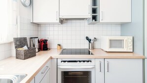 A modern kitchen with white cabinets, a microwave, a stove, and a clock on the wall. - Aldesago City View (Lugano)