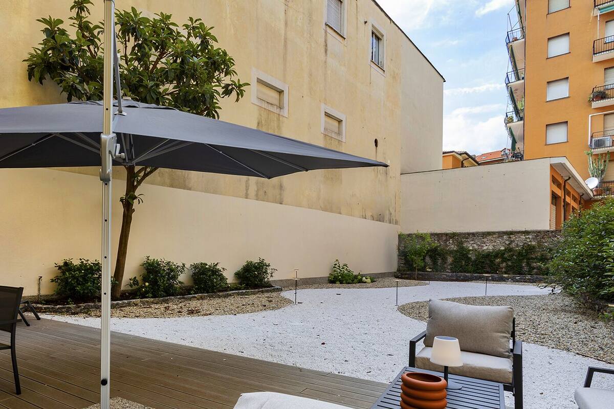 Une terrasse extérieure avec une table et des chaises, un grand parasol et un bâtiment en arrière-plan.