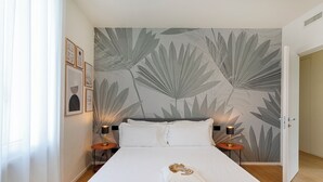 A hotel room with a large bed, two bedside tables with lamps, a wall with a leaf pattern, and a door leading to another room. - Riviera Flavour Apartments II by Wonderful Italy (Santa Margherita Ligure)