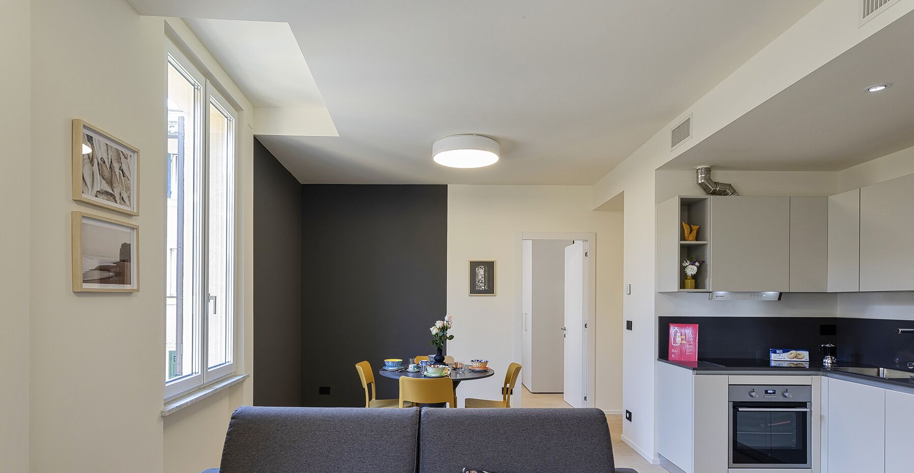 Une cuisine compacte dotée d’un four encastré, un coin repas avec une table et des chaises, et un canapé.
