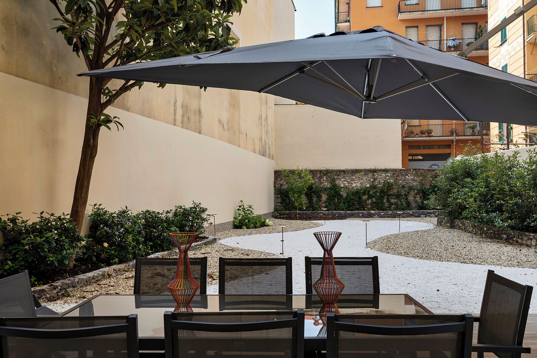 Une terrasse extérieure avec une table et des chaises, un grand parasol et un vase décoratif.