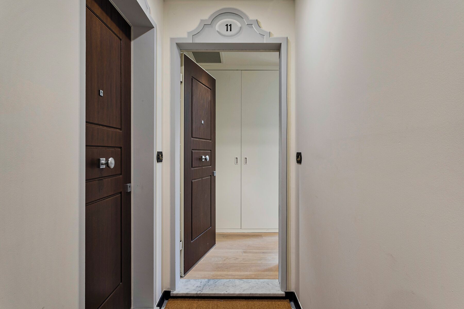 A hallway with a wooden door on the left and a white door with a number 11 sign above it.
