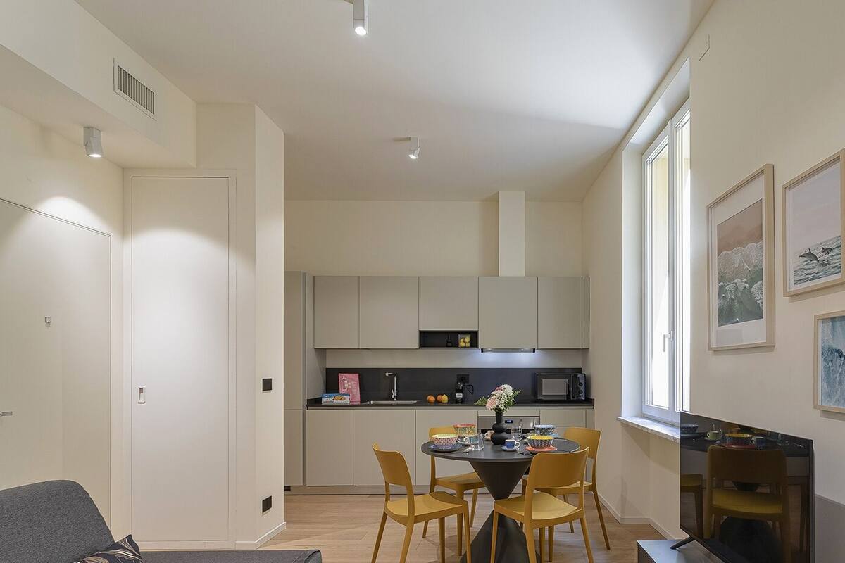 Une cuisine compacte dotée d’appareils électroménagers modernes, un coin repas avec des chaises jaunes et des œuvres d’art accrochées aux murs.