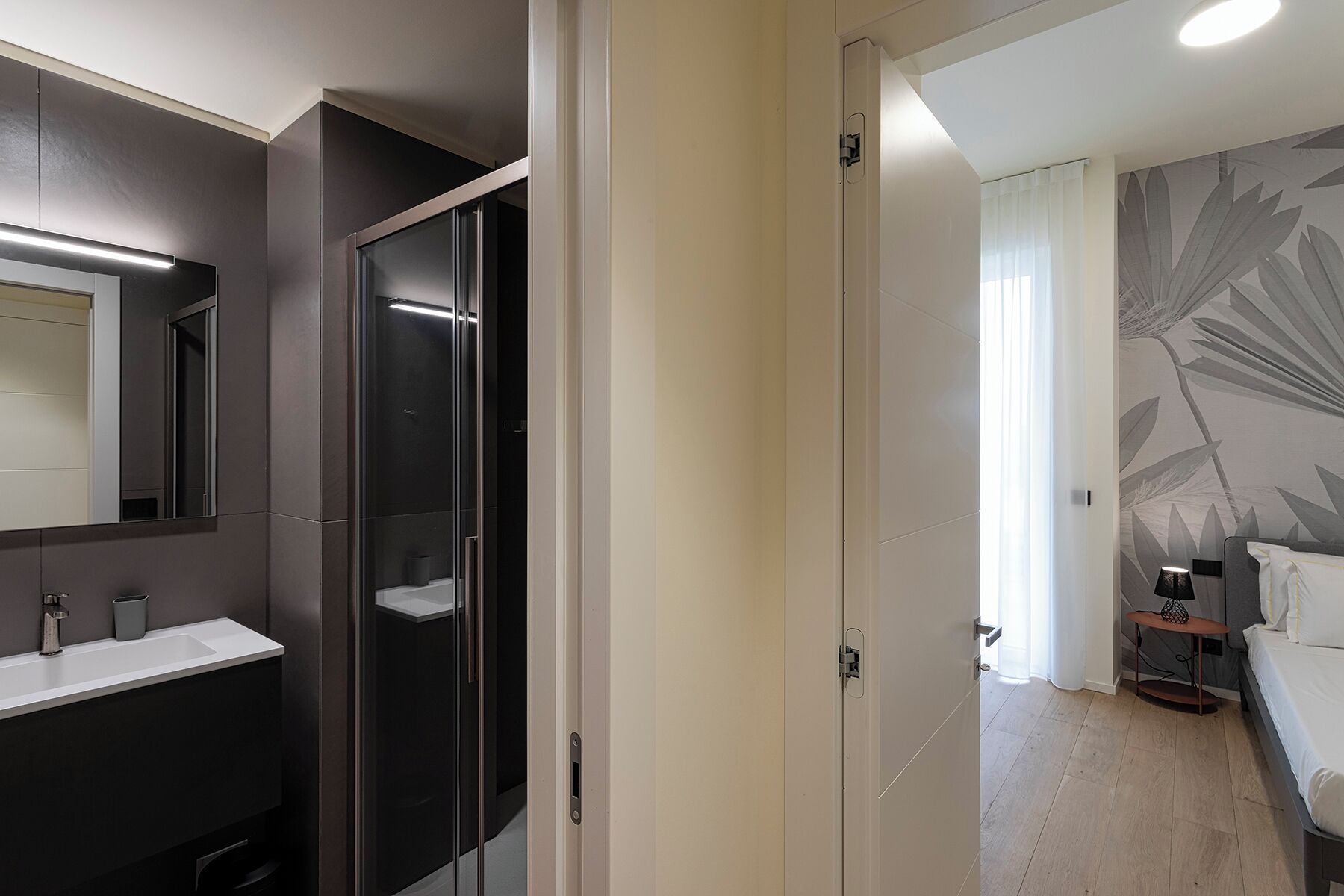 Un bagno moderno con doccia vetrata, uno specchio grande e un lavandino bianco.
