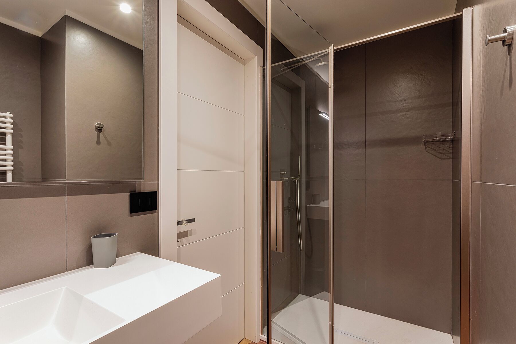A modern bathroom with a white sink, a glass shower enclosure, and a large mirror.