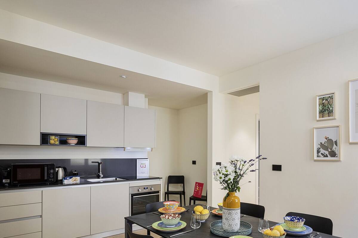 Une cuisine moderne avec des meubles blancs, un four à micro-ondes et un coin repas avec une table dressée pour deux personnes.