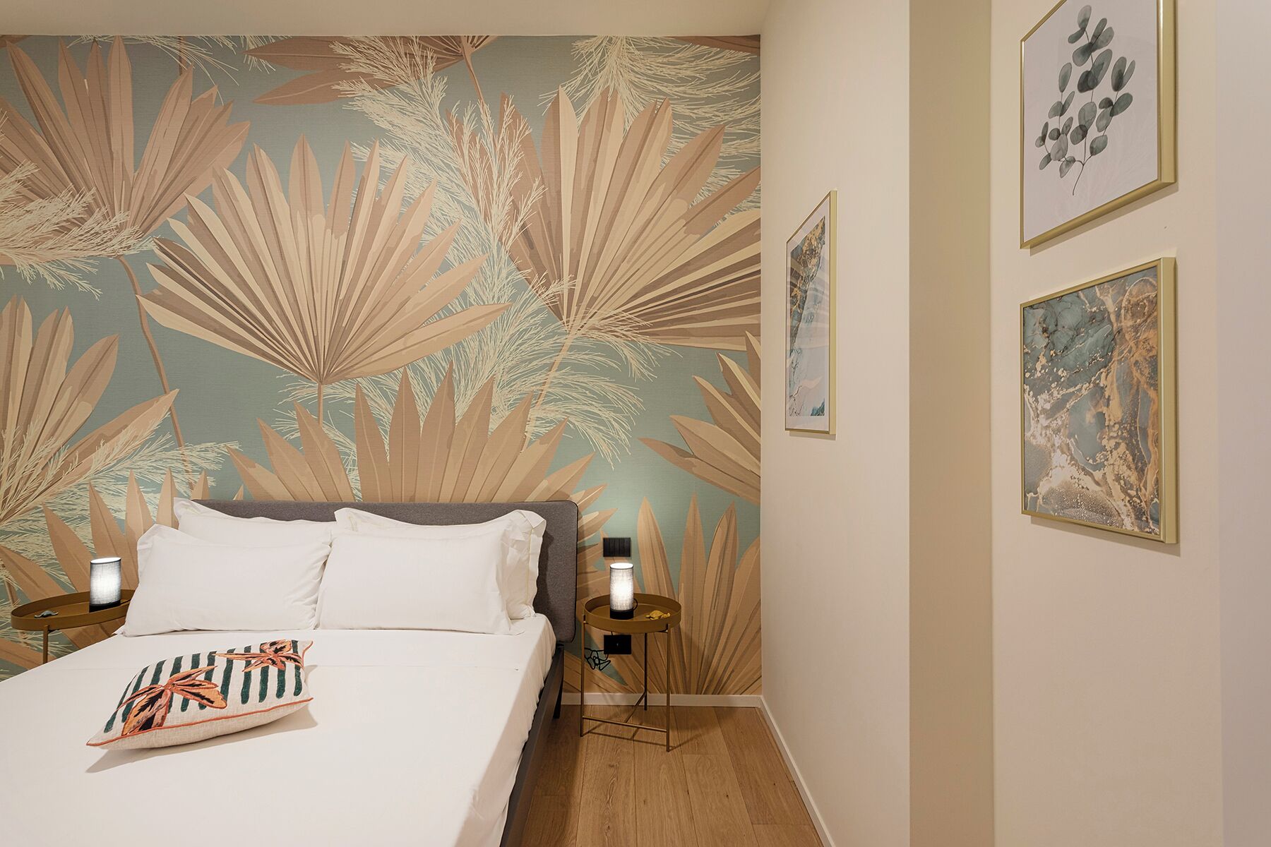 A bedroom with a bed, two bedside tables, a nightstand, and a wall with a tropical leaf pattern.