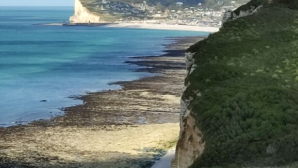 Paisagem costeira com falésias, uma praia e turbinas eólicas ao longe.