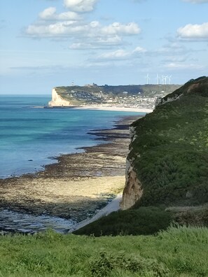 A coastal landscape with cliffs, a beach, and wind turbines in the distance. - Le Rayon Vert vue mer (Fécamp)