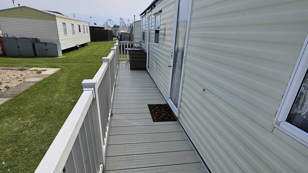 A narrow wooden deck leading to a mobile home with a white exterior and a chimney.