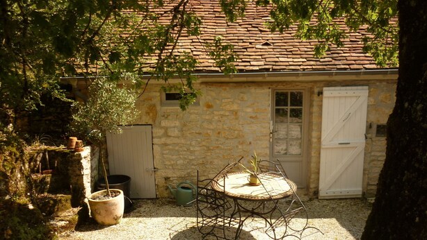 Un bâtiment en pierre avec un toit recouvert de tuiles, une table ronde en métal avec des chaises et une porte.