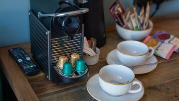 A coffee machine, cups, and a remote control on a wooden table.