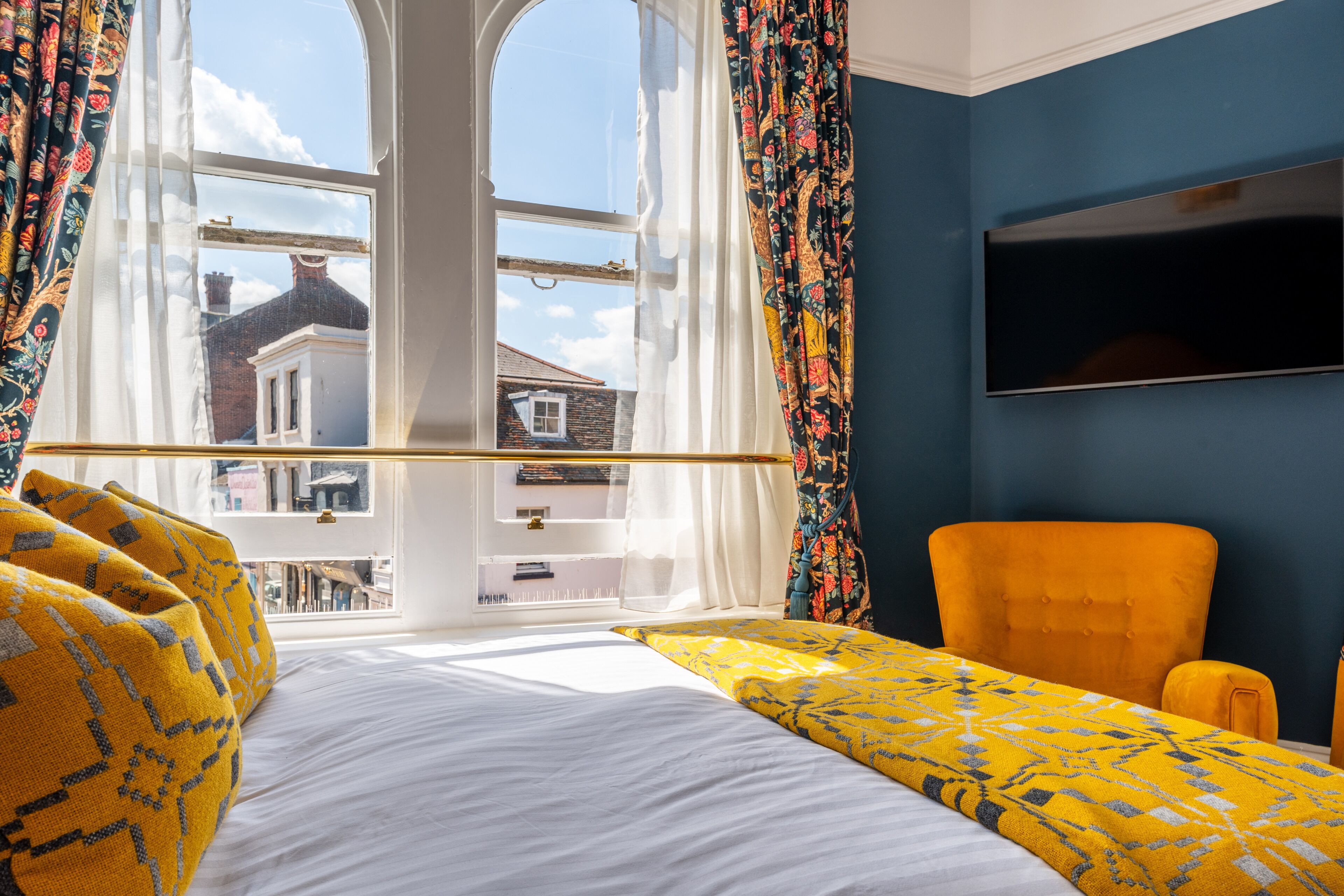 A room with a bed, a window with curtains, a television, and a chair.