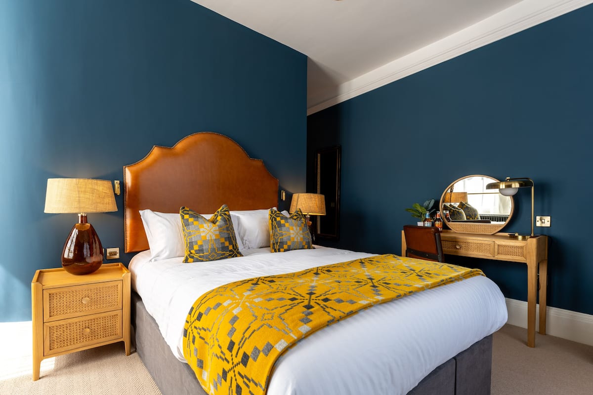 A neatly made bed with a wooden headboard, two bedside tables with lamps, a mirror, and a dresser.