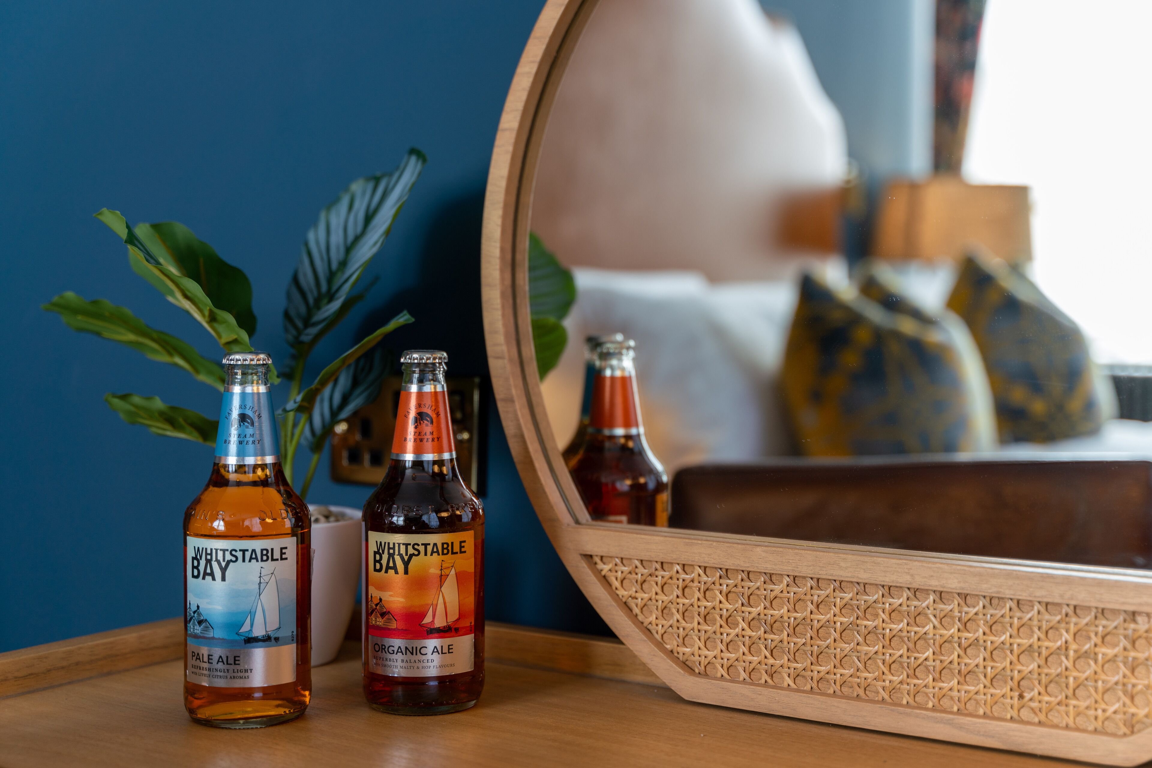 Two bottles of Whitstable Bay Pale Ale and Organic Ale on a wooden tray with a mirror reflecting a room.