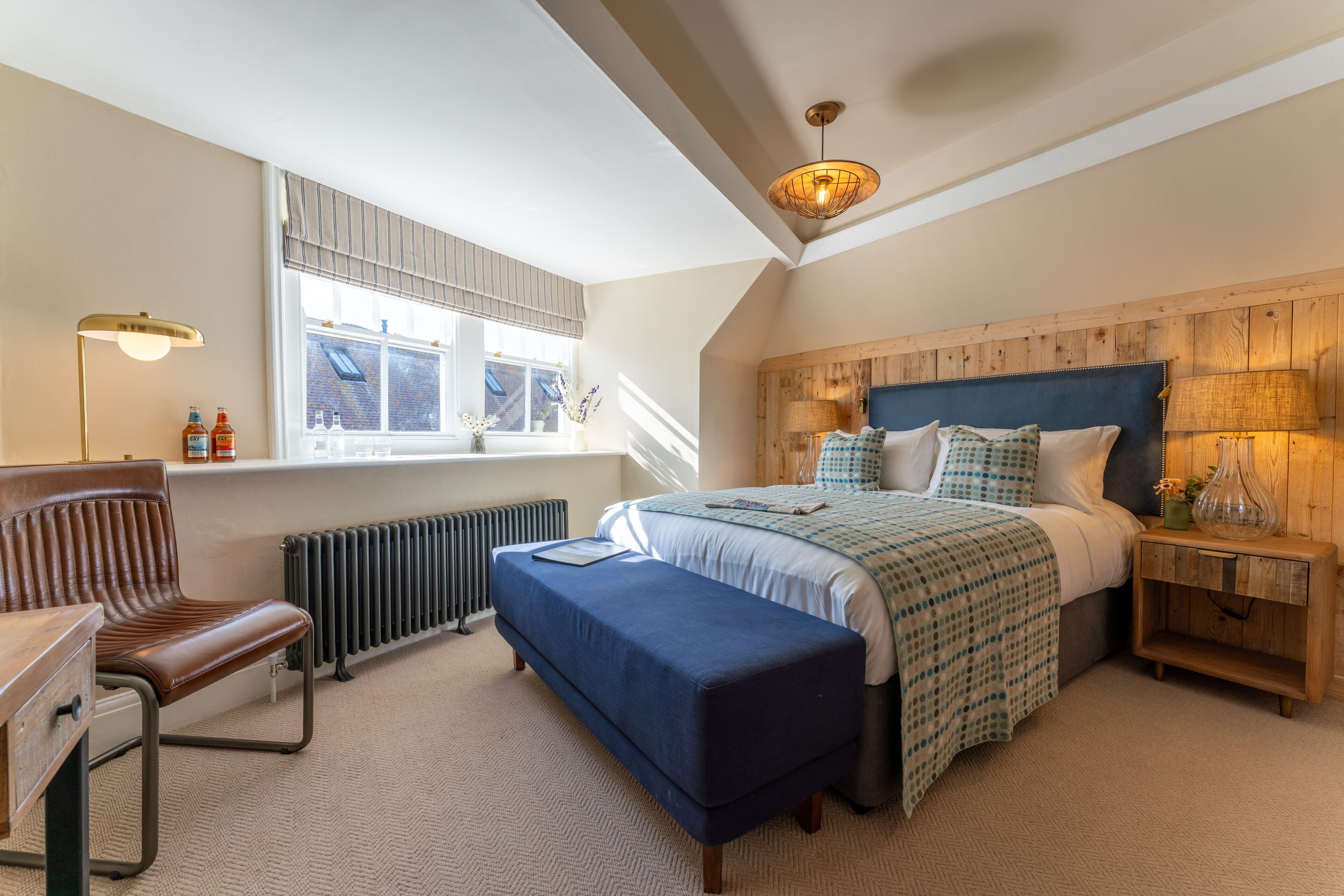 A bedroom with a large bed, a wooden headboard, a window with blinds, a desk with a chair, and a radiator.
