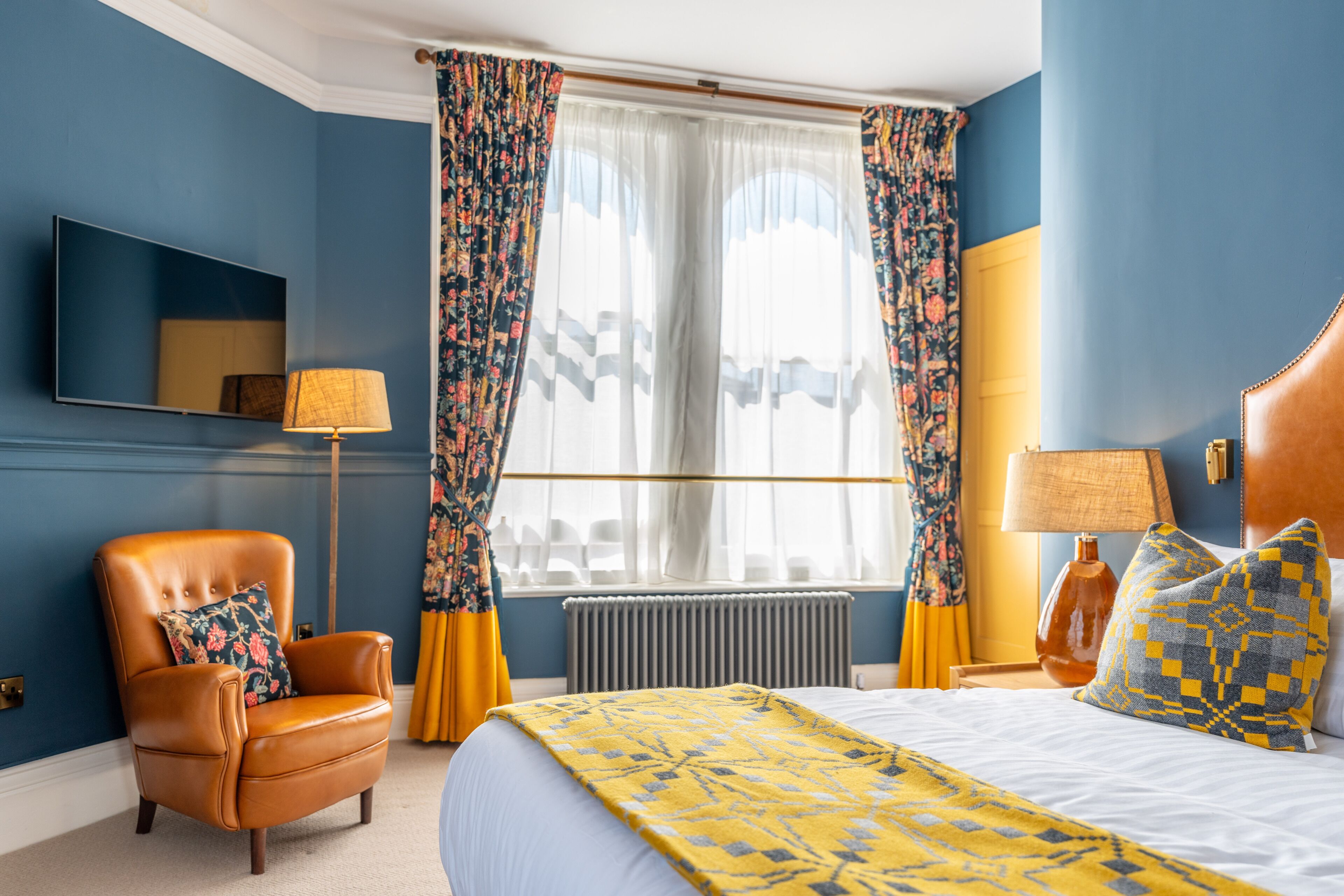 Une chambre d’hôtel avec un lit, une chaise, une lampe et des rideaux.