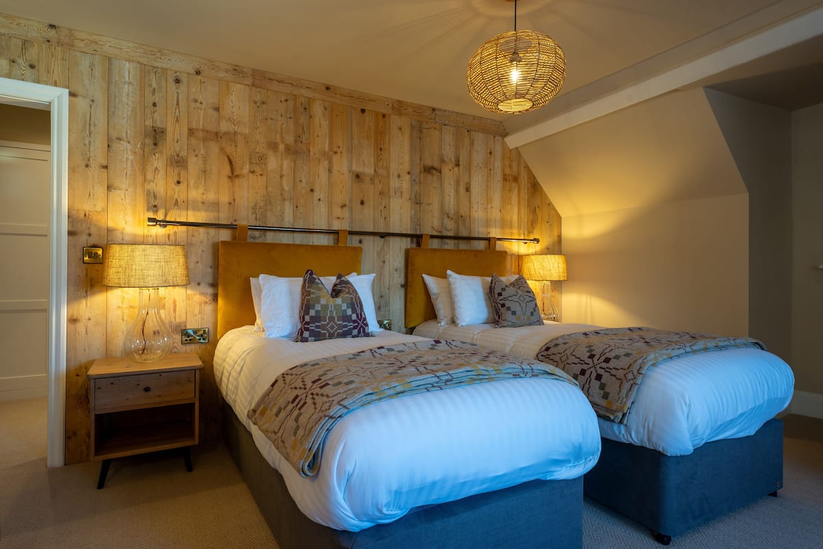 A bedroom with two beds, wooden paneling on the walls, and a hanging light fixture.