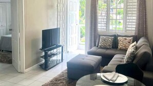 A living room with a sofa, ottoman, and a flat-screen TV on a stand. - Cozy Central 1-bed Apartment in Kingston (Kingston)