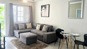 A modern living room with a grey sectional sofa, a small ottoman, a glass coffee table with chairs, and a ceiling fan. - Cozy Central 1-bed Apartment in Kingston (Kingston)