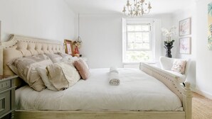 Ein Schlafzimmer mit einem großen Bett, einem Kronleuchter, einem Fenster und einem Sessel.