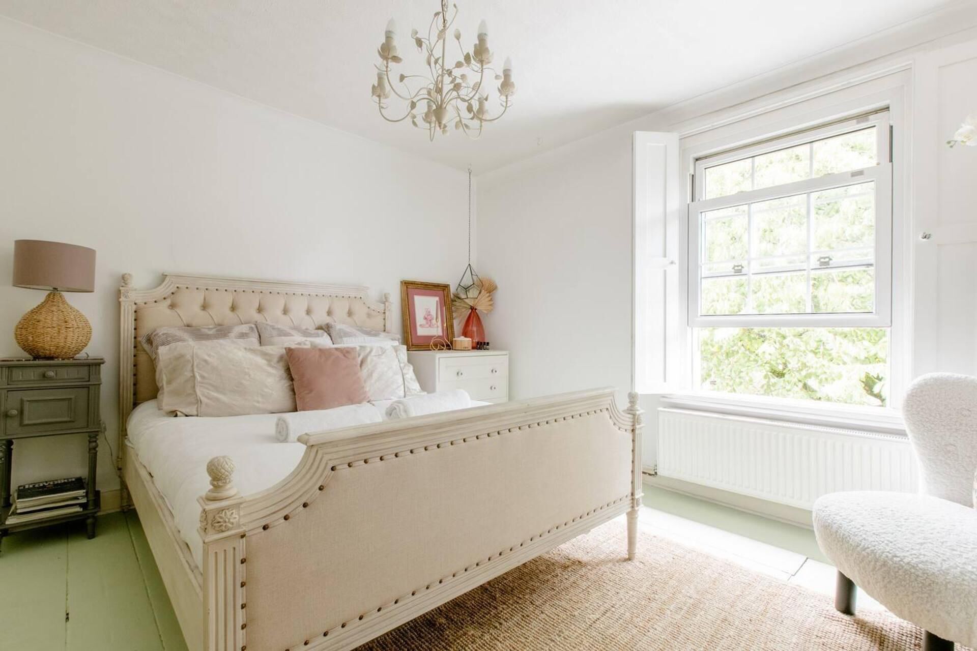 Un dormitorio con una cama grande, una mesita de noche, un aparador, una silla y una ventana con vistas al verdor.
