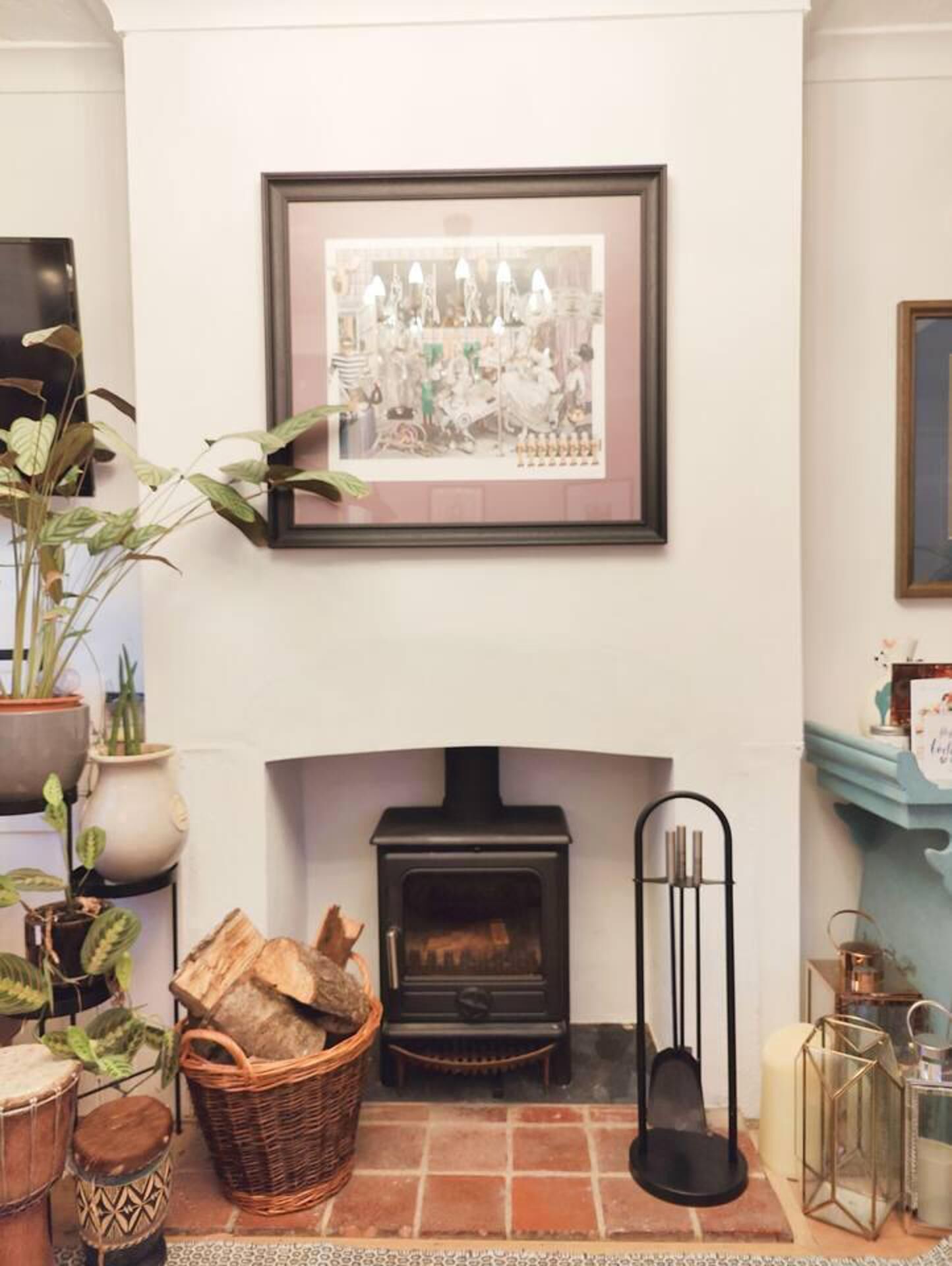 Un cuarto acogedor con chimenea, un cuadro enmarcado encima y diversos objetos decorativos, incluyendo plantas y velas.