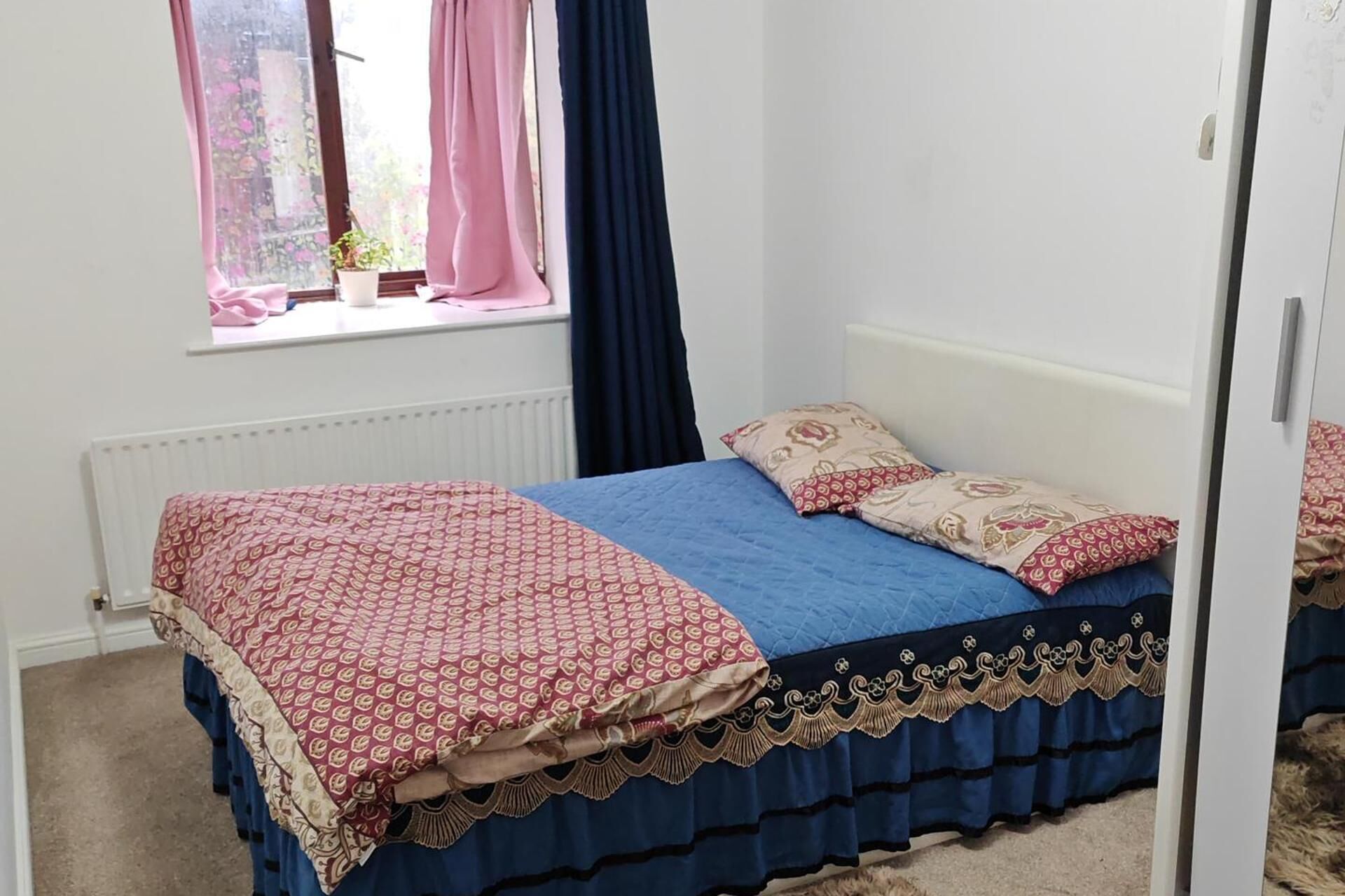 A bedroom with a bed, a window with curtains, and a radiator.
