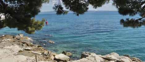 A rocky shoreline with clear blue water and a red buoy in the distance.