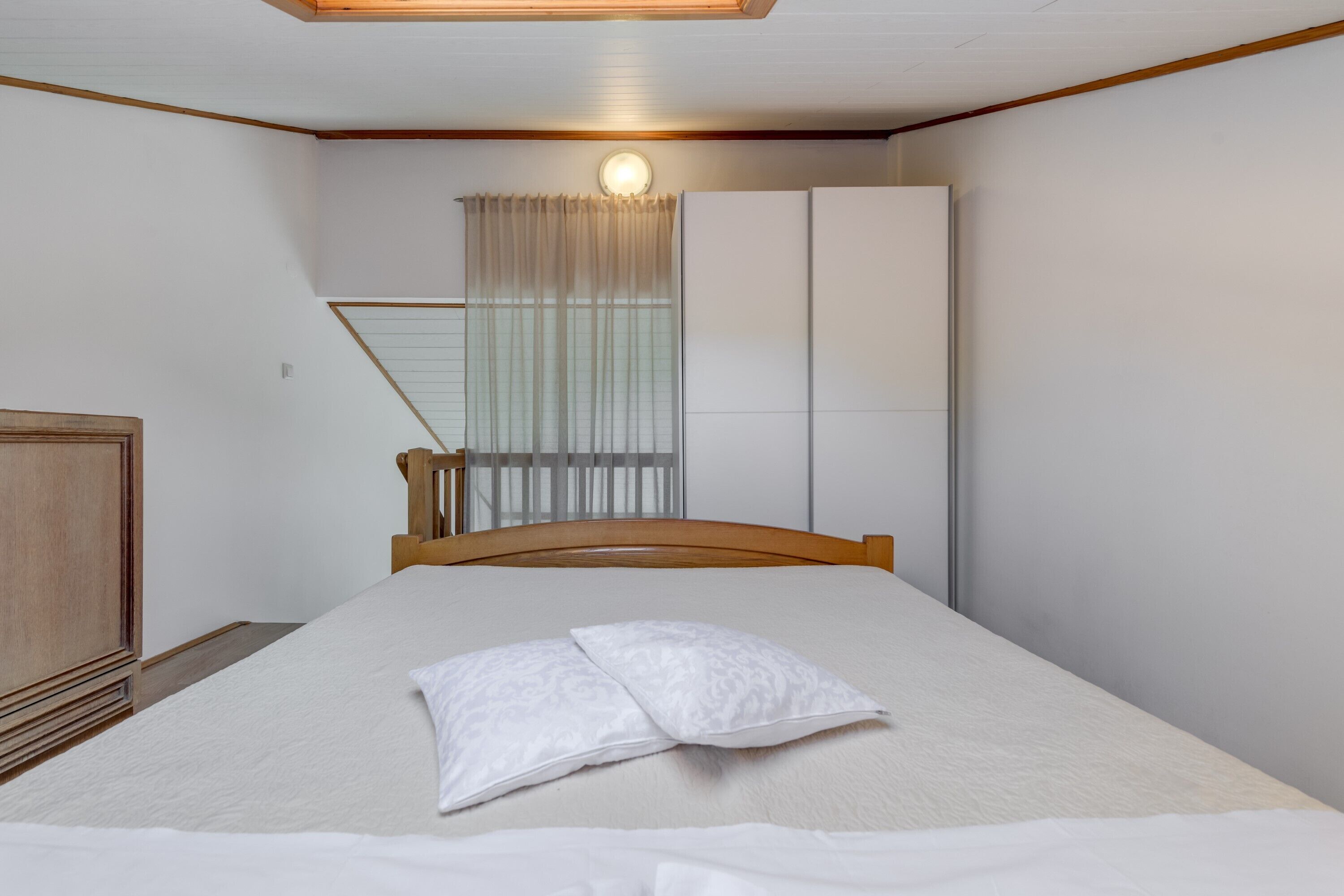 A bedroom with a bed, a wooden headboard, a wardrobe, and a window with curtains.