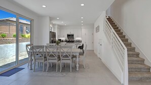 A modern kitchen with white cabinets, a central island, and a dining area with a table and chairs. - Brand New at PGA West, views, community pool, sleeps 10 #254654 (La Quinta)
