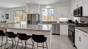 A modern kitchen with white cabinets, a granite countertop, a stainless steel refrigerator, and a built-in oven. - Brand New at PGA West, views, community pool, sleeps 10 #254654 (La Quinta)