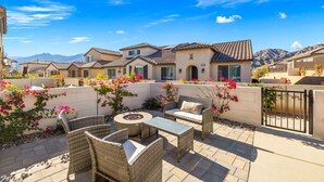 A patio area with wicker furniture and a fire pit, surrounded by a white wall and flowering plants. - Brand New at PGA West, views, community pool, sleeps 10 #254654 (La Quinta)