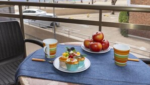 Ein Balkon mit Tisch, gedeckt für eine Mahlzeit, mit Blick auf einen Strand und einen Parkplatz.