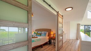 Une chambre à coucher avec un lit, une table de chevet, une lampe et une vue sur l’extérieur.