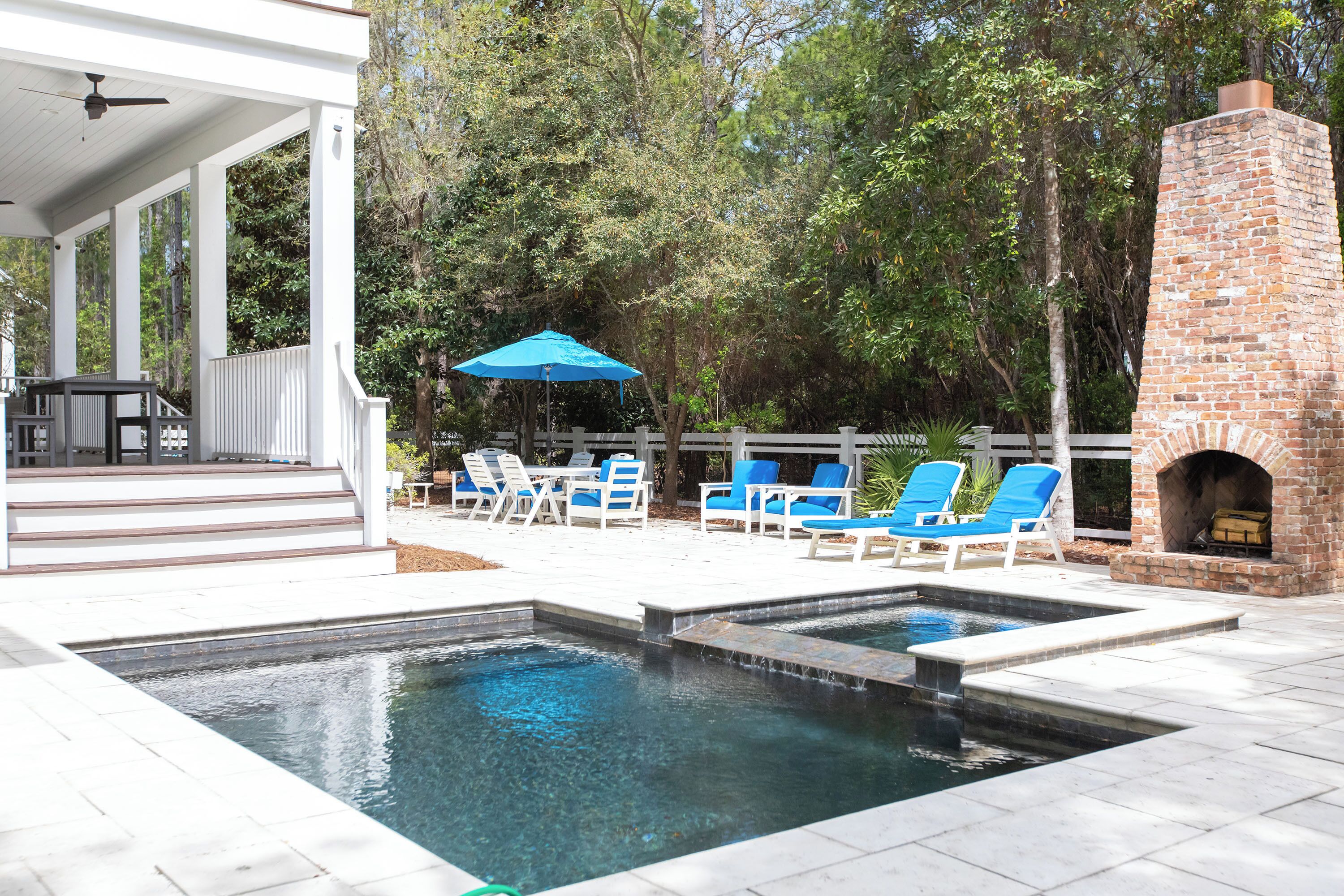 A swimming pool with a brick fireplace and lounge chairs.