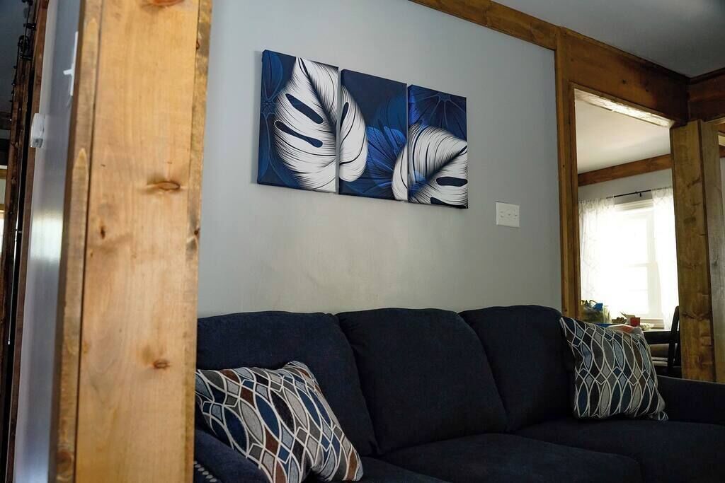 A room with a dark blue sofa, two patterned throw pillows, and a wall-mounted abstract painting.