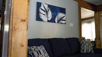 A room with a dark blue sofa, two patterned throw pillows, and a wall-mounted abstract painting.