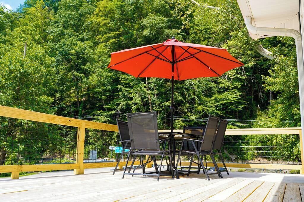 Une terrasse en bois, agrémentée d’une table et de chaises, entourée d’une rambarde jaune, et offrant une vue sur une zone boisée.
