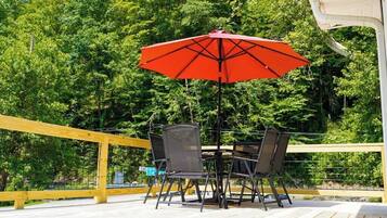 Une terrasse en bois, agrémentée d’une table et de chaises, entourée d’une rambarde jaune, et offrant une vue sur une zone boisée.