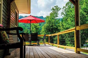 A wooden deck with a red umbrella, a black chair, and a table. - *The Decked out Den* (Delbarton)