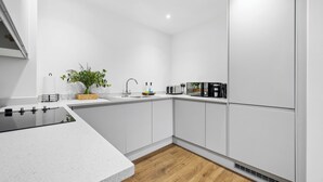 A modern kitchen with white cabinetry, a black countertop, a sink, a microwave, and a small plant.