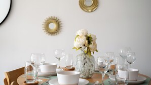 A dining table set with white plates, bowls, and clear wine glasses, with a vase of white flowers in the center.