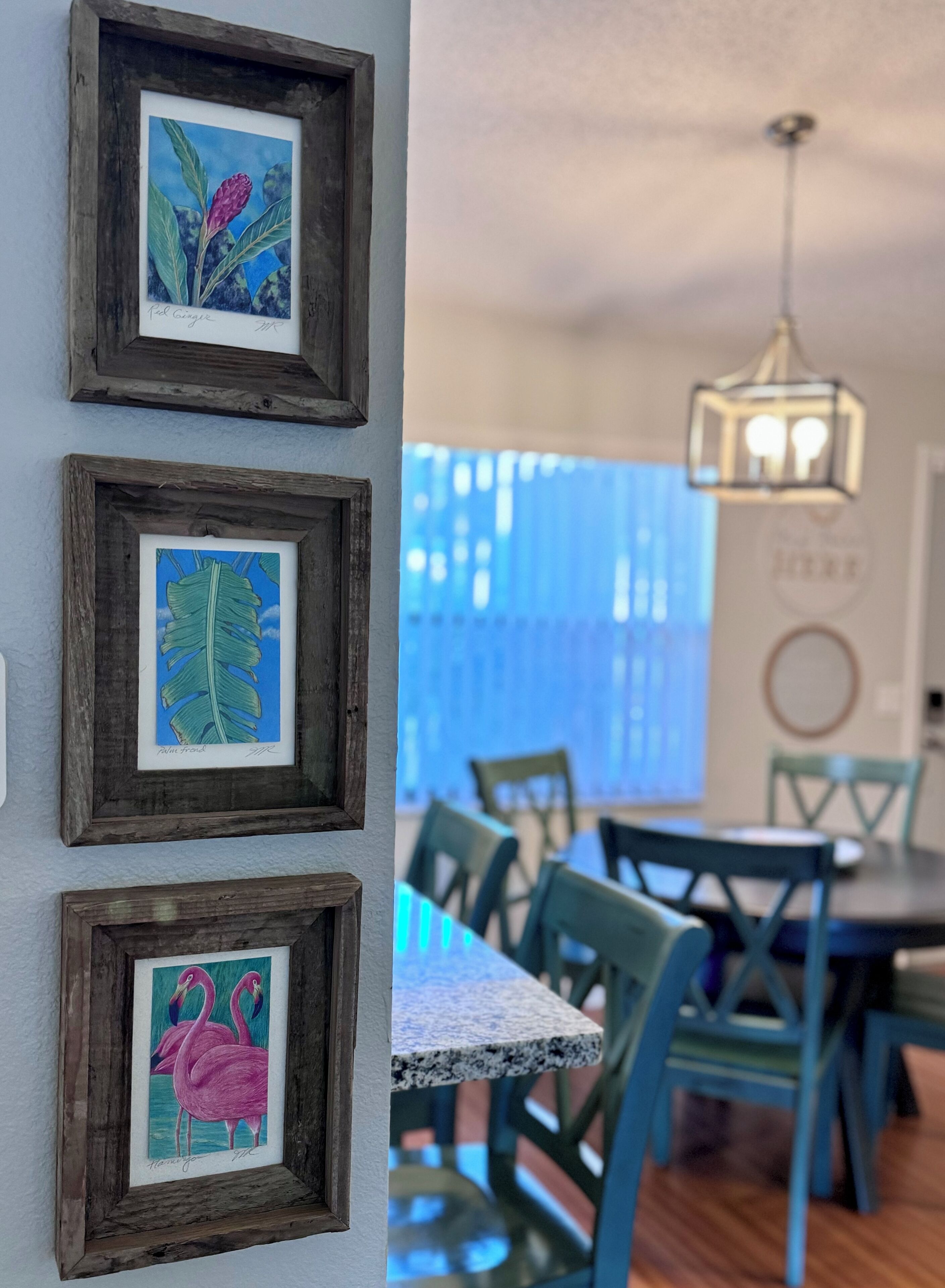 A dining area with a table and chairs, framed artwork on the wall, and a hanging light fixture.