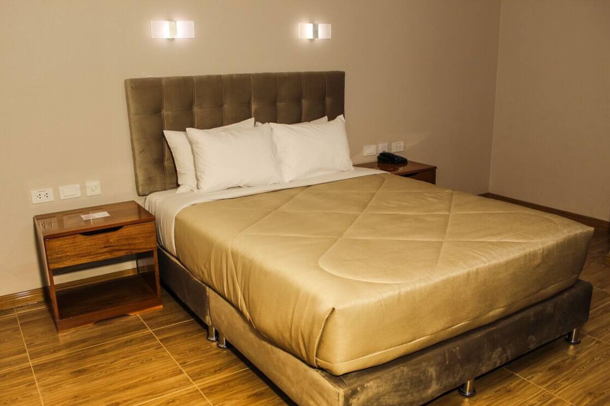 Un dormitorio con una cama grande, una mesita de noche de madera y una mesita auxiliar.