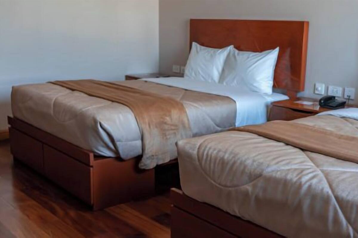 Dos habitaciones de hotel contiguas con cabeceras de madera, ropa de cama blanca y suelo de madera.
