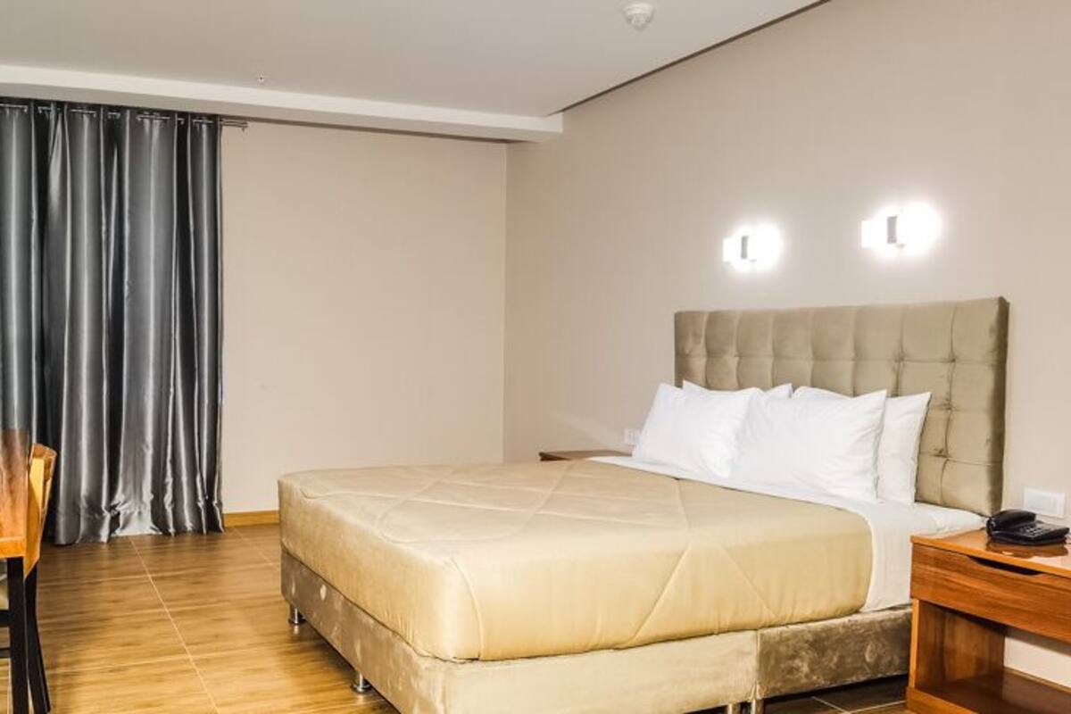 Habitación de hotel con cama, escritorio, silla, televisión y ventana con cortinas.