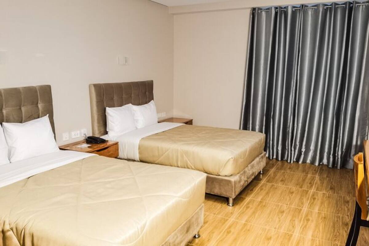 Una habitación de hotel con dos camas, un escritorio de madera y un gran ventanal con cortinas.