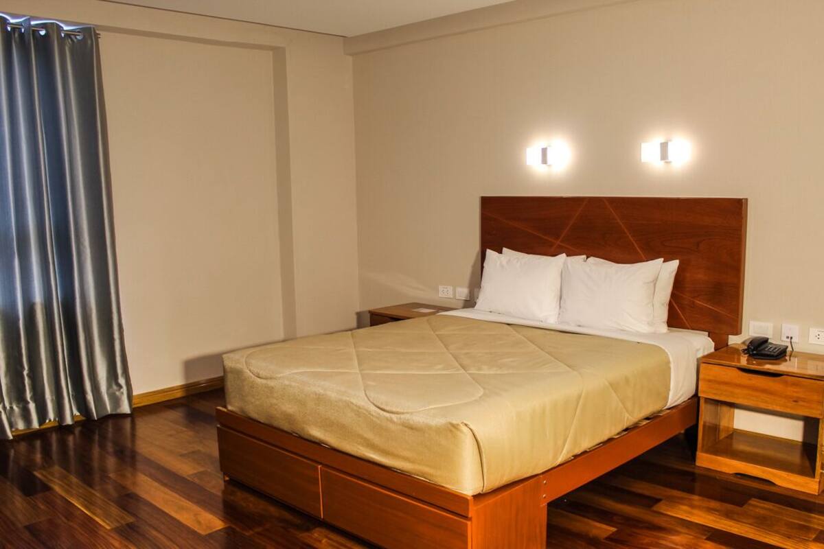 Una habitación de hotel con una cama de madera, una mesita de noche con un teléfono y una cortina.