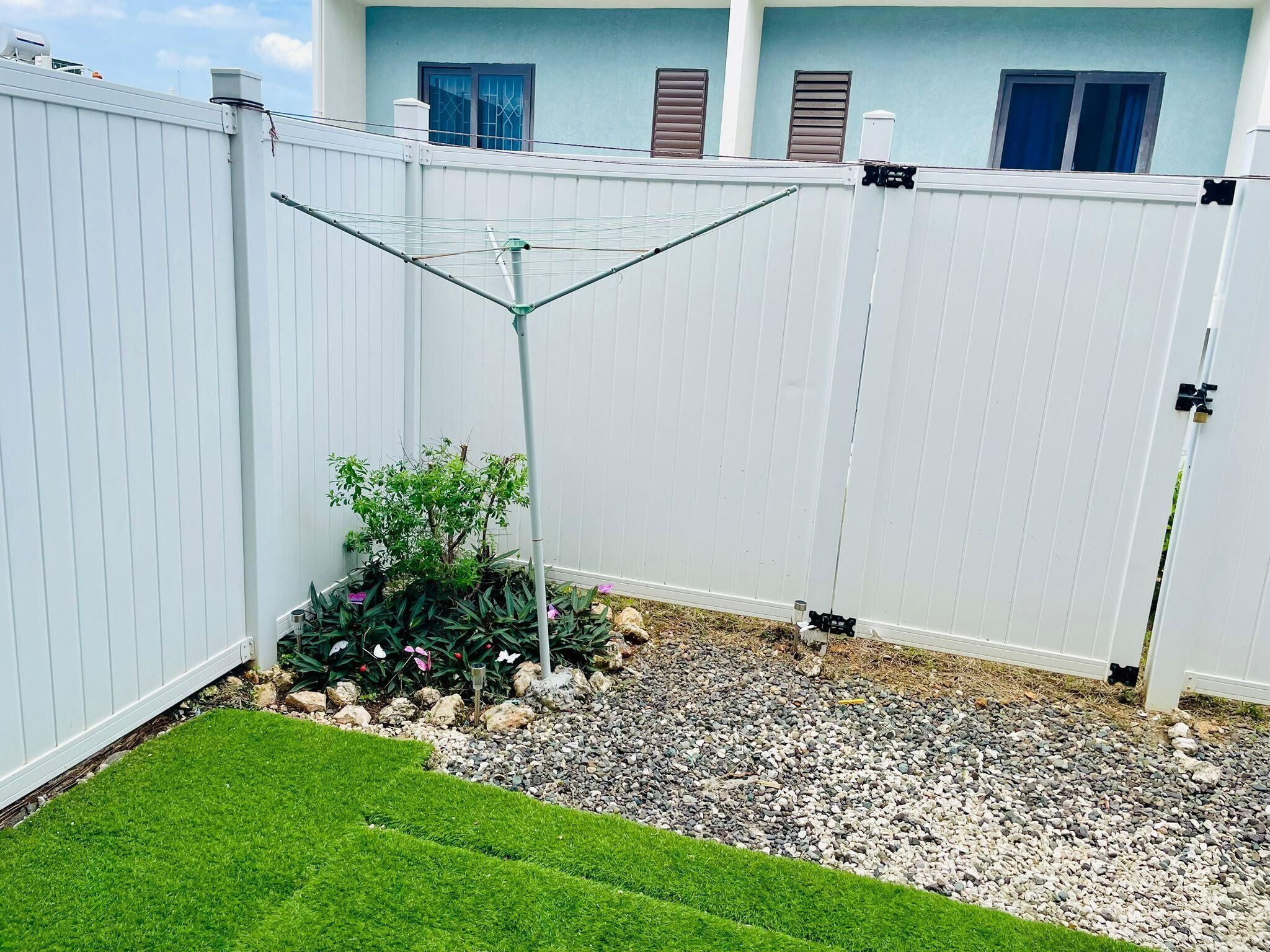 A fenced backyard with a small garden area, a metal structure, and a dog peeking from behind the fence.